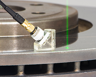 Laserstrahl und Sensor auf einer beschichteten Bremsscheibe. Forscher am Fraunhofer IWS haben gezeigt, dass eine schnelle und zerstörungsfreie Bewertung mit dem LAwave®-Verfahren möglich ist.