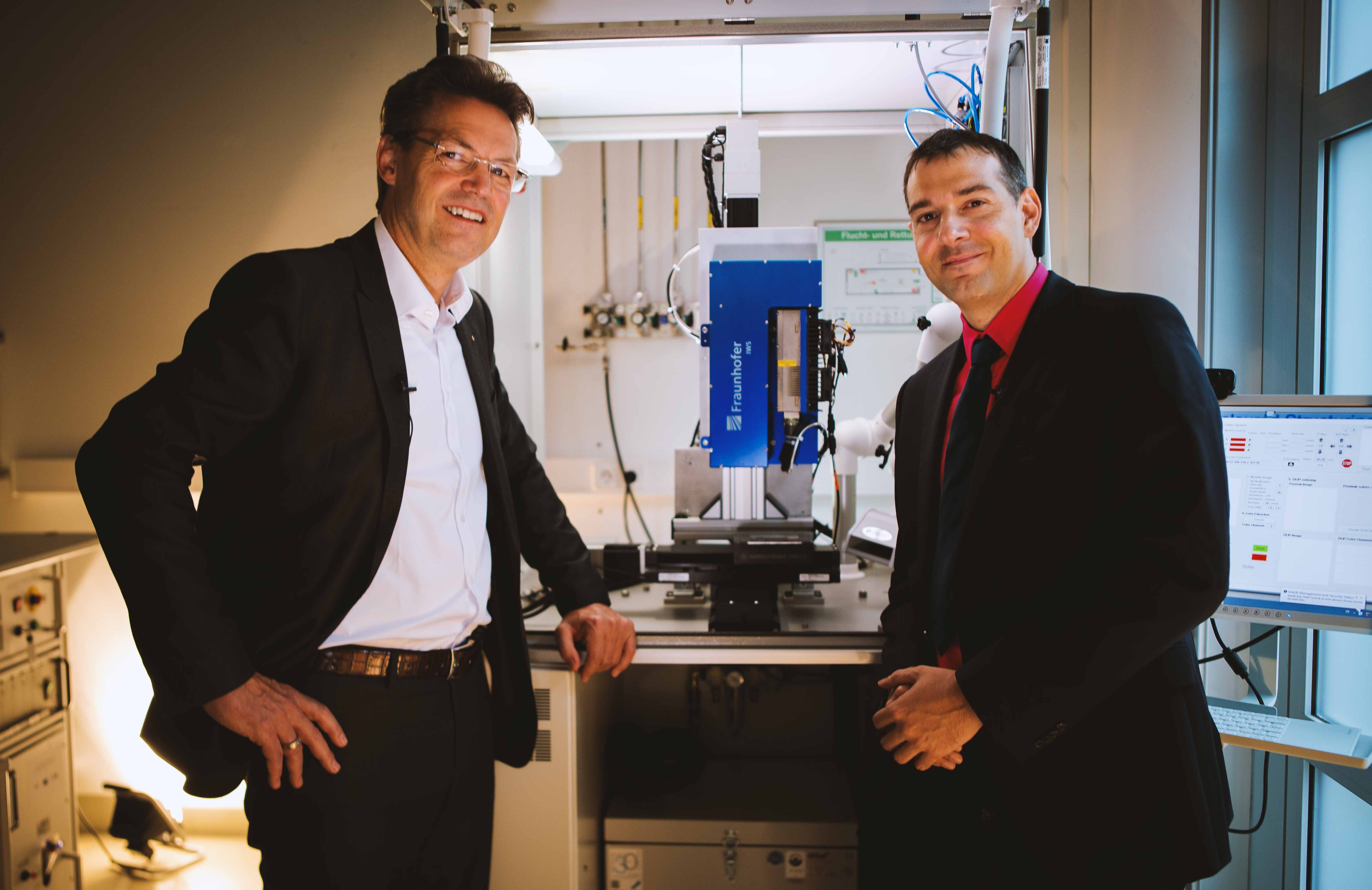 Prof. Frank Mücklich (links) und Prof. Andrés F. Lasagni (rechts) vor einer am Fraunhofer IWS entwickelten DLIP µFAB-Anlage
