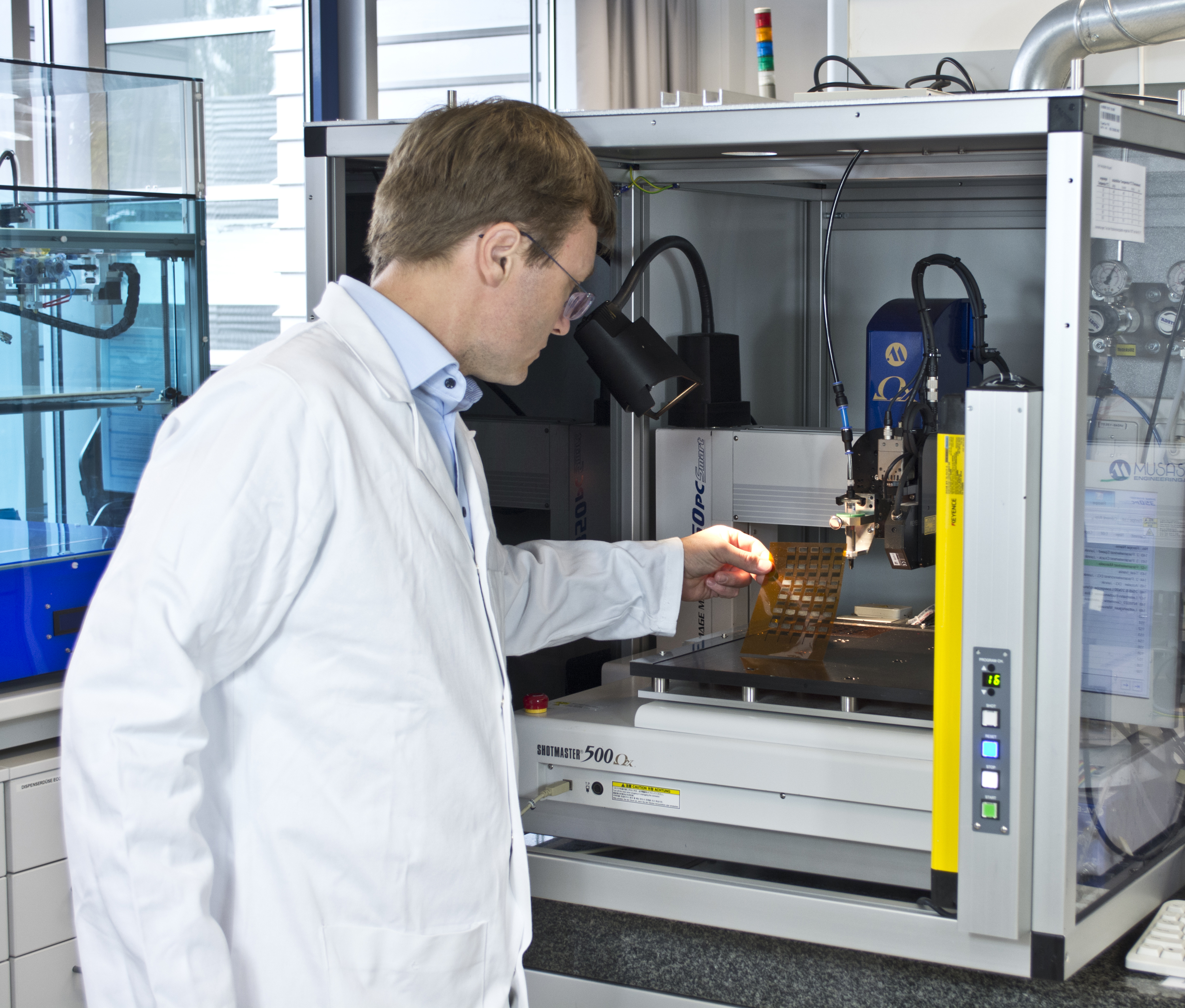 Dr. Roman Tkachov examines a film printed with two different conductive polymers at a dispensing printer in the Fraunhofer IWS Dresden. "PEDOT:PSS" is a polymer with positive charge carriers (“p-conductive”), while “Poly(Kx[Ni-itto])” transports negative charge carriers (“n-conductive”). This also shows that IWS polymers can be processed using standard techniques such as printers or rotary coating.