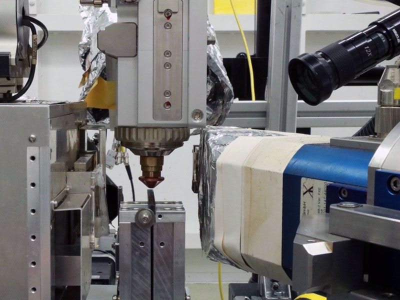 Experimental setup in the Fastshape project for high-speed in-situ process monitoring in laser beam cutting with dynamic beam shaping. An X-ray source with detector to visualize the cutting front geometry and a polarization goniometer to determine the melt flow are used as analysis devices.